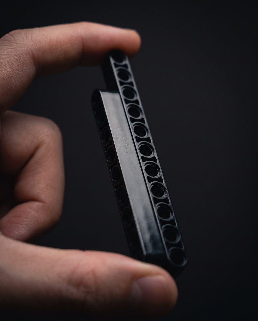 Macro of a single black technic beam held between two fingers under soft studio light